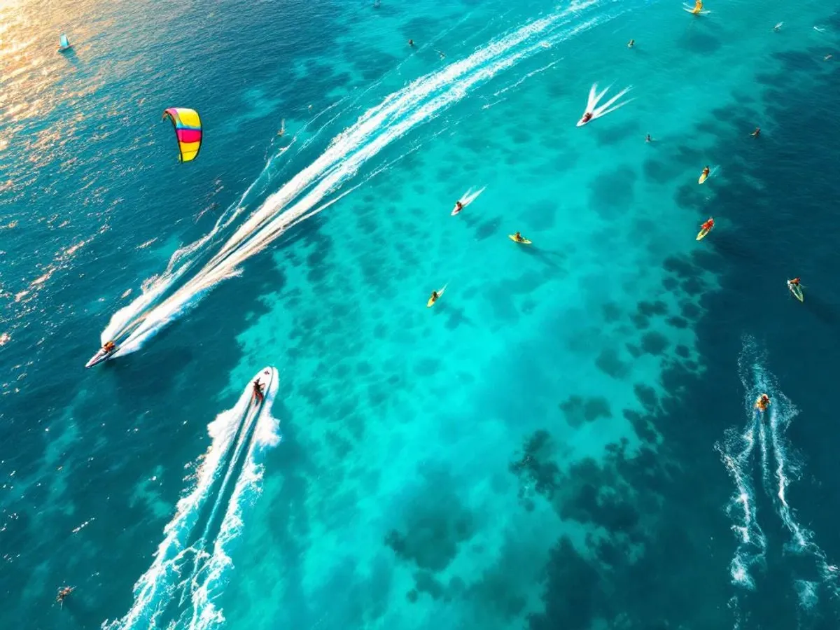 Luchtfoto van turquoise water met watersporters: wakeboarden, kitesurfen, paddleboarden en jetskiën bij zonsondergang