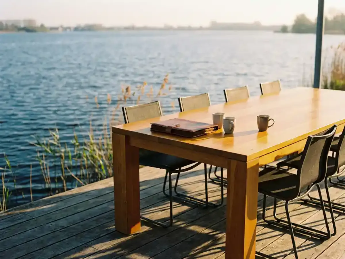 Houten vergadertafel op terras aan het Eemmeer met lege stoelen, portfolio en koffiekopjes, riet aan waterkant