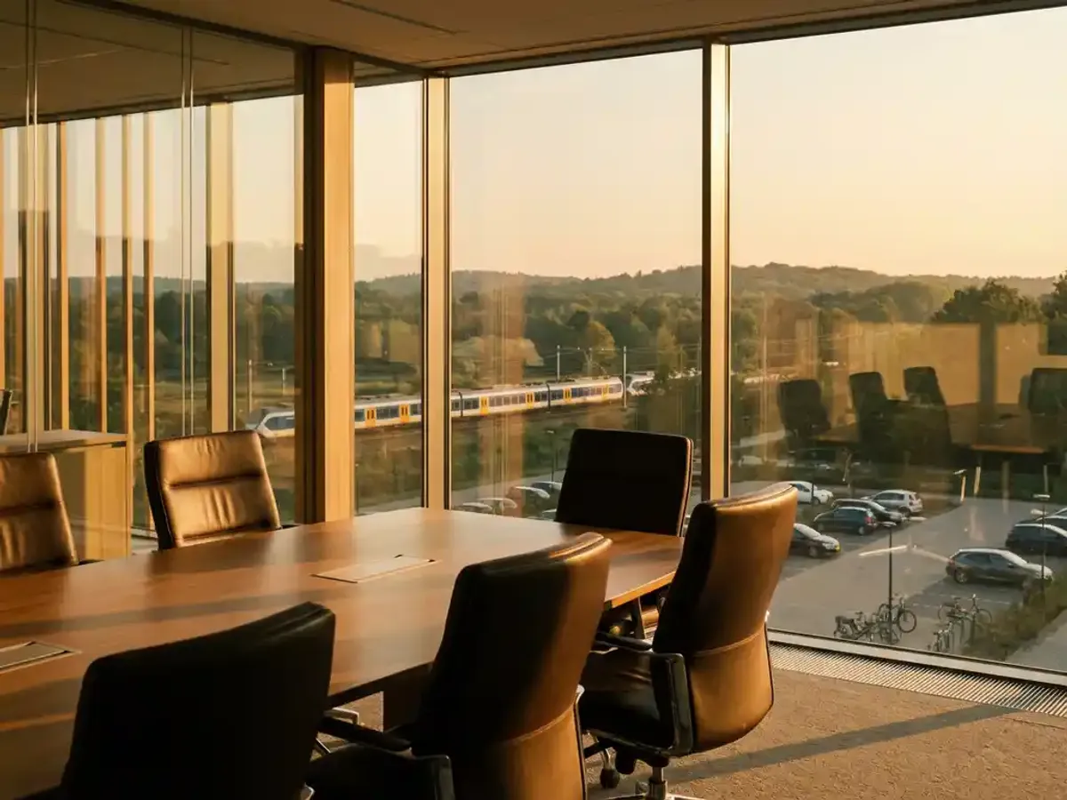 Moderne vergaderzaal met leren stoelen rond houten tafel, uitzicht op Utrechtse Heuvelrug met trein in landschap