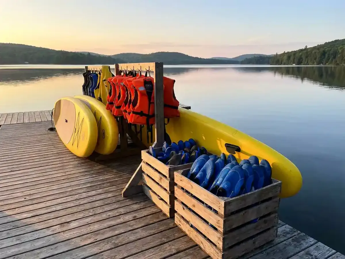 Kleurrijke watersportuitrusting op houten steiger met gele paddleboards, oranje zwemvesten en blauwe waterschoenen